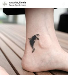 a small dolphin tattoo on the foot of a woman's leg, with her feet crossed