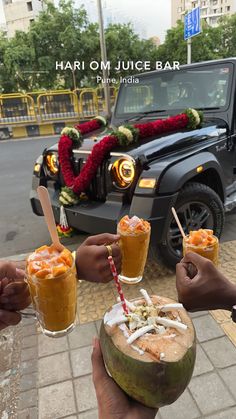 four people holding up drinks in front of a jeep with flowers on the street behind them