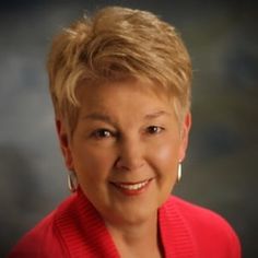 a woman with blonde hair wearing a red sweater and gold hoop earrings smiles at the camera