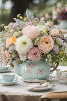 a tea pot filled with lots of flowers on top of a table next to cups and saucers