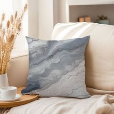 a white and blue pillow sitting on top of a couch next to a coffee cup