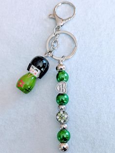 a keychain with a doll and beads attached to it on a white surface