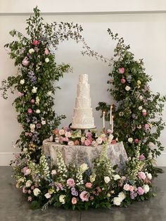 a wedding cake sitting on top of a table surrounded by flowers and greenery with candles