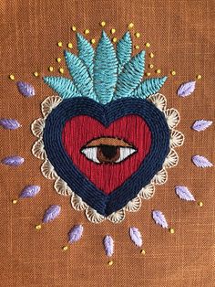 a heart with an eye and leaves on it is embroidered onto the side of a piece of fabric