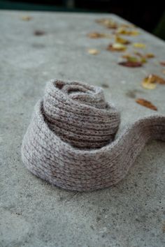 a gray knitted scarf laying on top of a cement slab with leaves scattered around it