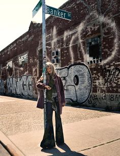 a woman standing next to a street sign in front of a graffiti covered brick building