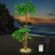 a palm tree is lit up with green lights on the beach at night, next to a remote control