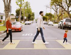 a man and woman walking across a crosswalk with a small child in front of them