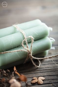 three green candles tied with twine on top of a wooden table next to nuts