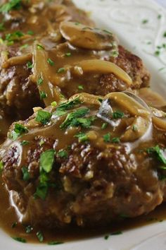 two meatballs covered in gravy on a white plate with green garnish