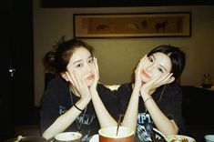 two young women sitting at a table with food and drinks in front of their faces