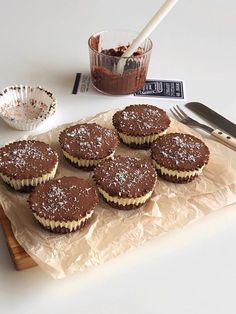 four chocolate cupcakes are sitting on a tray next to a knife and fork