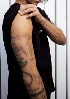 a man with many tattoos on his arm and shoulder is standing in front of a white wall