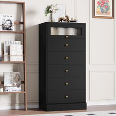 a black chest of drawers next to a book shelf with books on it and pictures above