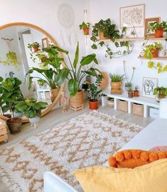 a living room filled with lots of potted plants next to a white couch and round mirror