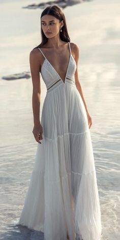 a woman standing in the water wearing a white dress with spaghetti straps and an open back