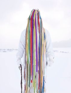 a man with long colorful hair standing in the snow wearing a white shirt and tie dye dreadlocks on his head