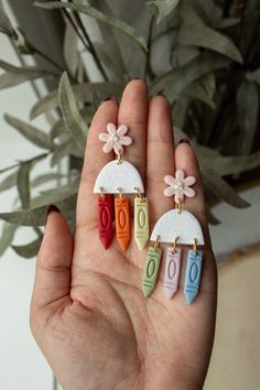 a person holding three different colored earrings in their hand with flowers on the top and bottom