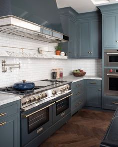 a kitchen with blue cabinets and white marble counter tops, an oven and stove hood