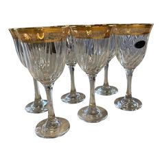 four wine glasses sitting next to each other on top of a white surface with gold trimming