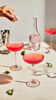 a table topped with three wine glasses filled with pink liquid and garnished with mint