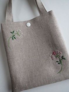 a gray bag with flowers embroidered on the side and a white button in the middle