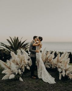 a bride and groom kissing in front of some pamolite plants with the ocean in the background