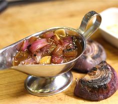 a metal bowl filled with stew next to garlic and an onion on a wooden table