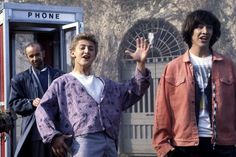 two young men standing in front of a phone booth, one holding his hand up