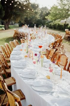 a long table is set up with white plates and place settings for an outdoor dinner