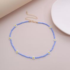 a blue and yellow beaded necklace next to a white plate on a pink surface