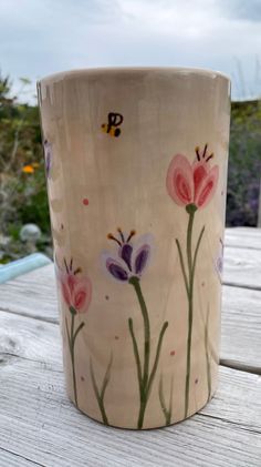 a cup with flowers painted on it sitting on top of a wooden table next to grass