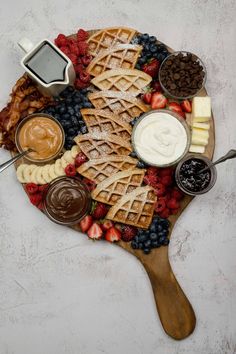 a wooden platter with waffles, fruit and dips on it next to chocolate sauce