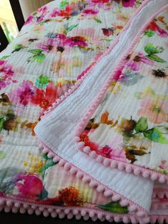 a pink flowered bedspread with pom - poms on the edges