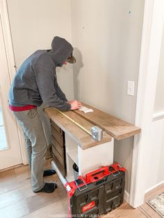 a man in grey hoodie working on a table with drawers and toolboxs