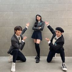 three young people posing in front of a wall with their hands out to the side