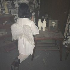 a woman sitting at a table with angel wings on her back and an old photo in the background