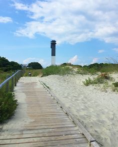 a wooden walkway leading to a light house on the beach with grass and trees in the background