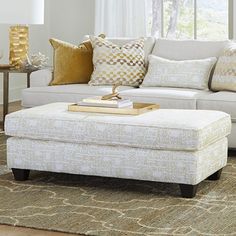 a living room with white couches and pillows on top of the floor, in front of a window