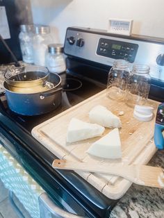 cheese is sitting on a cutting board next to an oven with pots and pans