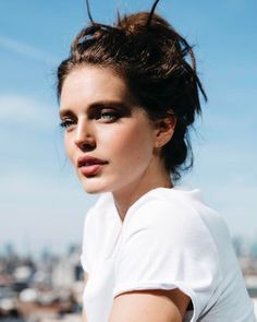 a woman with her hair in a bun is looking at the camera while wearing a white t - shirt