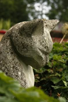 a stone cat statue sitting in the bushes