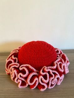 a crocheted red and pink hat sitting on top of a wooden table