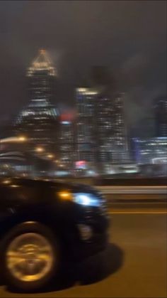 a blurry image of a car driving down the road in front of a cityscape