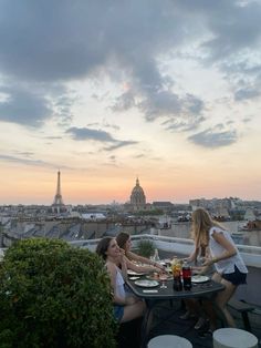 three women sitting at a table on top of a roof with the eiffel tower in the background