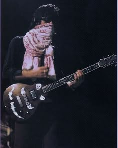 a man with long hair playing an electric guitar in front of a microphone and wearing a bandana