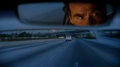 the reflection of a man's face in a rear view mirror on a highway