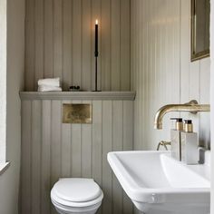 a white toilet sitting next to a bathroom sink under a mirror in a room with wood paneling