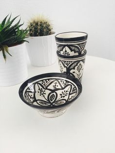 three black and white bowls sitting on top of a table next to potted plants