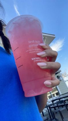 a woman holding up a pink drink in her hand